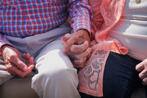 Free Crop unrecognizable aged couple in casual clothes sitting close and holding hands while spending time together Stock Photo