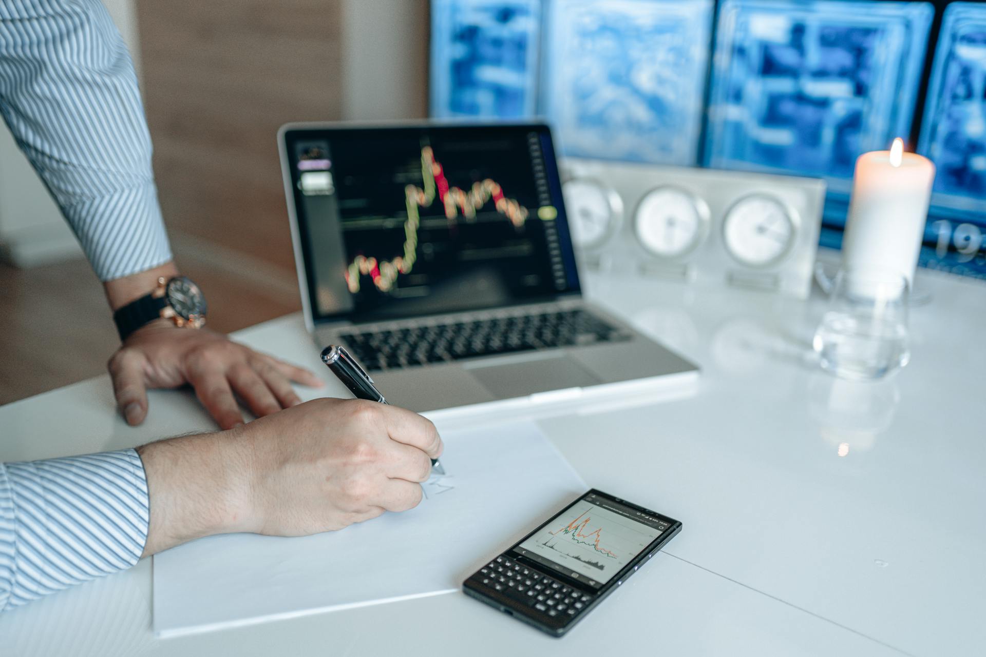 Man analyzing stock market trends on a laptop, writing notes on paper.