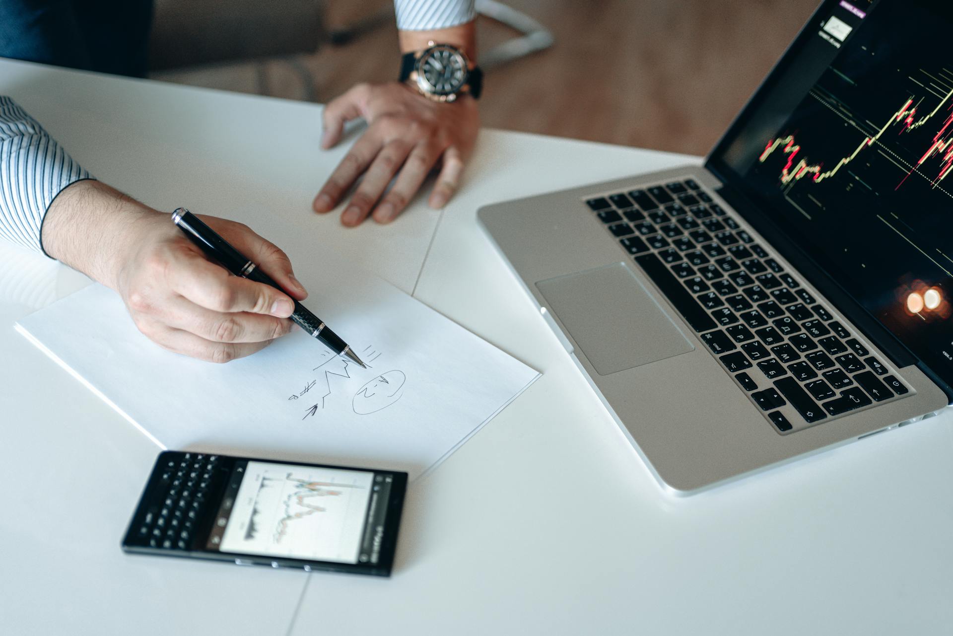 Professional workspace with financial analysis on laptop, smartphone, and paper.