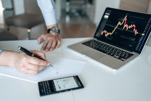 Professional workspace featuring laptop with stock charts, smartphone, and paper for business analysis.