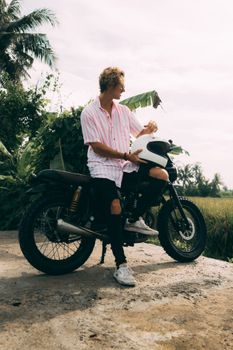 一名戴头盔的男子骑着摩托车，穿行在巴厘岛户外的热带风景中
