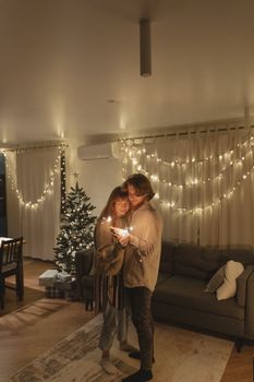 一对夫妇在灯光温暖、挂着圣诞树的客厅里，用烟花庆祝新年