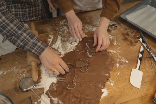 Free Two people using cookie cutters on dough, baking cookies with various kitchen tools. Stock Photo