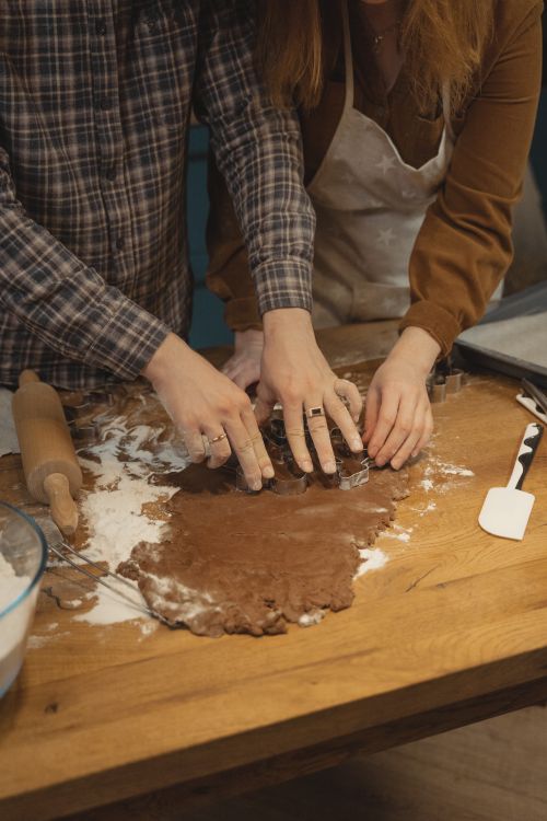 Free A couple preparing dough for baking on a wooden surface with a rolling pin and spatula. Stock Photo