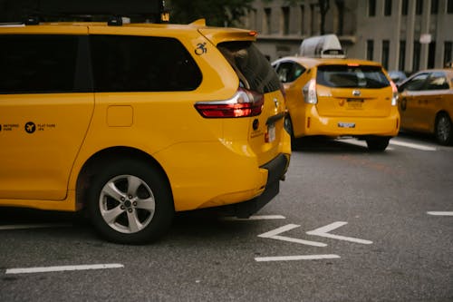 Modern yellow crossover taxi cars riding on asphalt road near commercial buildings in city