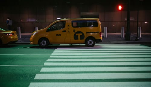 Comfortable yellow minivan cab parked on city asphalt road near traffic light at night