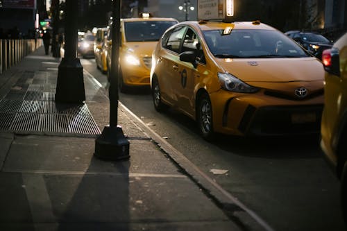 Stylish yellow taxi car riding on asphalt road near sidewalk in modern city district in evening