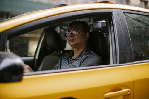 Serious ethnic man driving yellow cab on city street