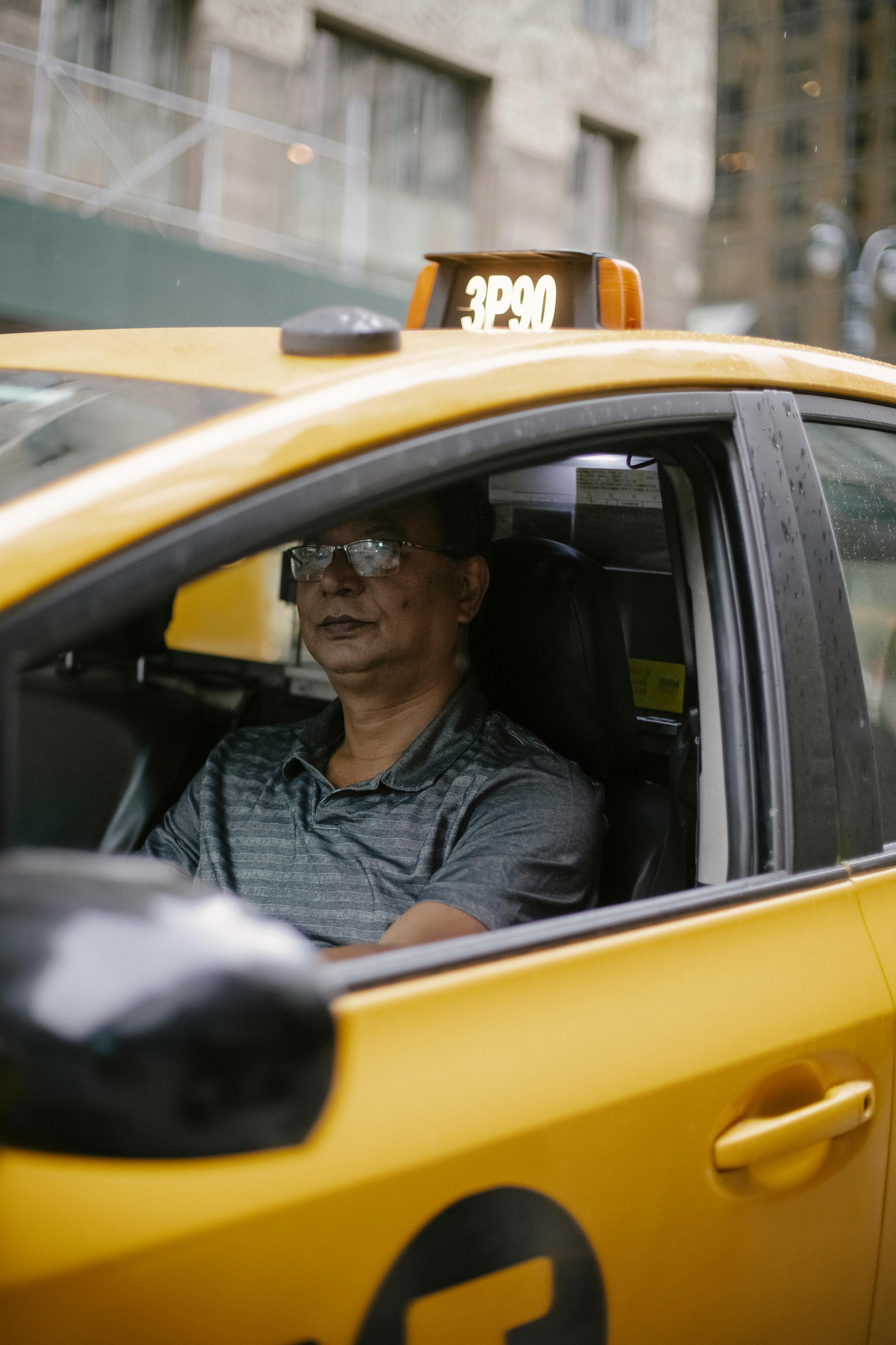 attentive ethnic male driver in yellow cab on city street