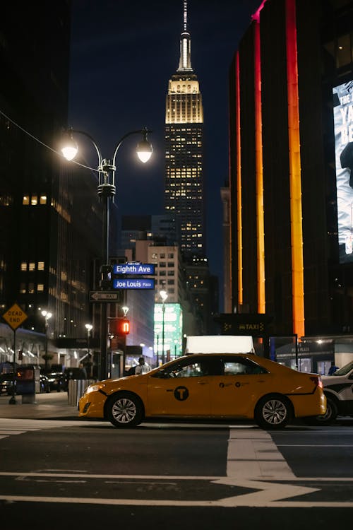 Free Contemporary yellow sedan taxi car stopped at zebra crossing near illuminated skyscraper in New York City at night Stock Photo