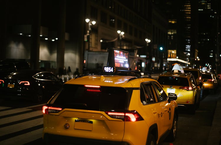 Hatchback Taxis Driving On City Street At Night