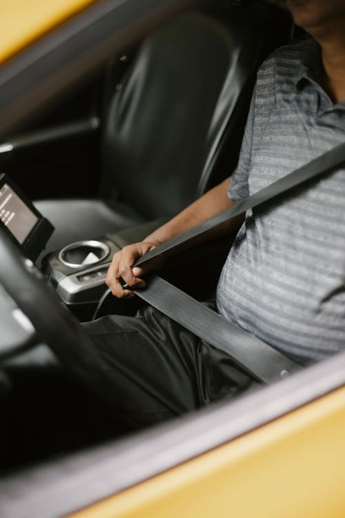 From above of crop unrecognizable male driver fastening seat belt while sitting in car in daytime