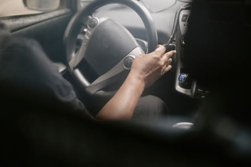 High angle of crop unrecognizable male driving modern car on street on sunny day