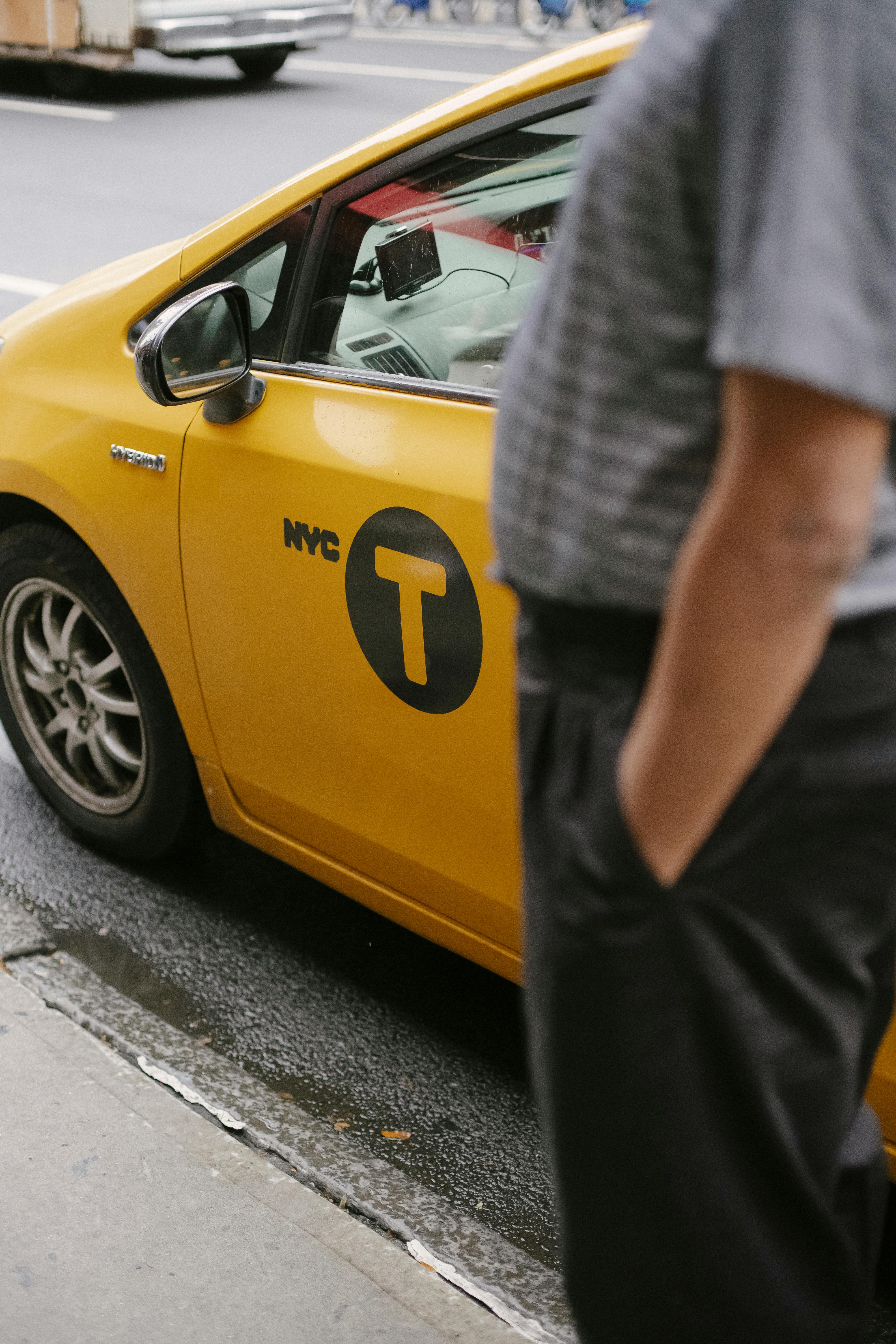 man with hands in pocket waiting near yellow taxi