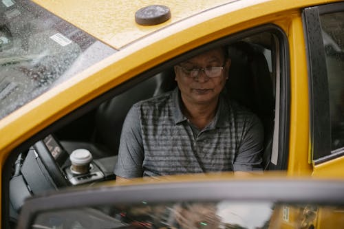 From above of focused Asian taxi driver sitting in wet car with opened door and looking down