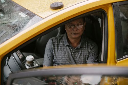 Free From above of focused Asian taxi driver sitting in wet car with opened door and looking down Stock Photo