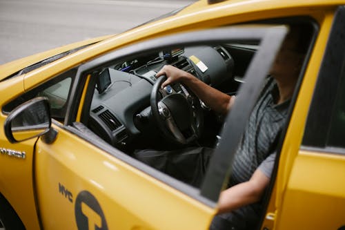 Free From above of anonymous man holding steering wheel and sitting in yellow car on road in daytime Stock Photo