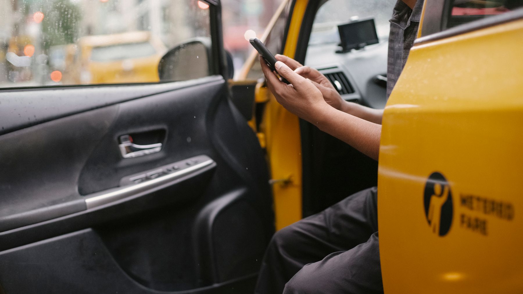 Side view of anonymous driver using smartphone and sitting in yellow automobile in city
