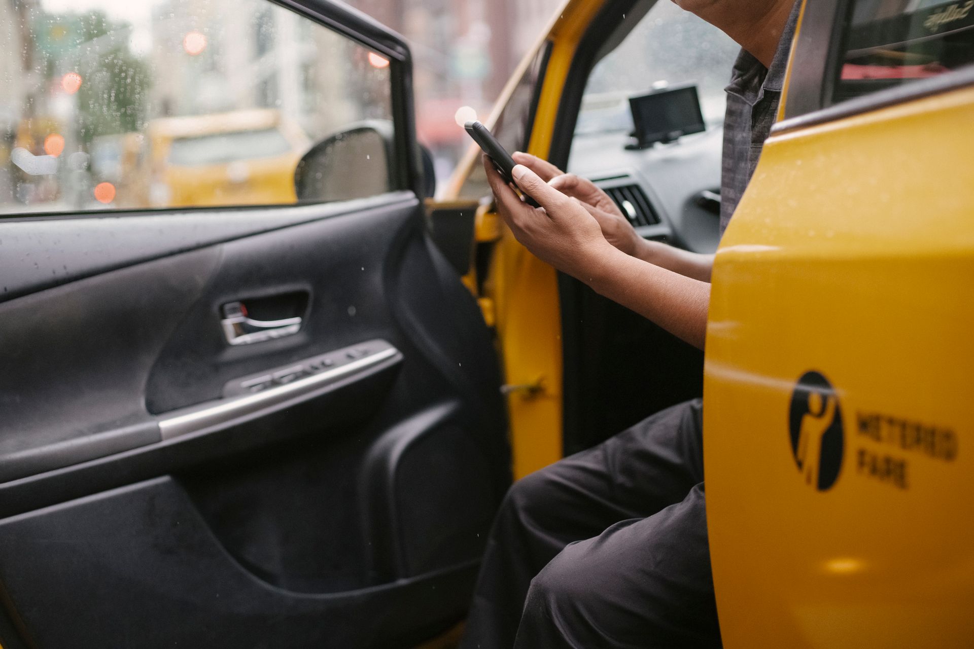 Man using smartphone inside a taxi in an urban environment with city street view.