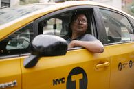 Serious taxi driver in glasses sitting in yellow automobile and looking up on street in city in daytime