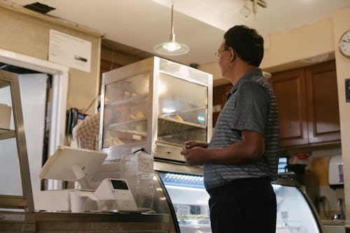 Free Side view of ethnic male wearing casual clothes standing near showcase and cash register while buying food in grocery store Stock Photo