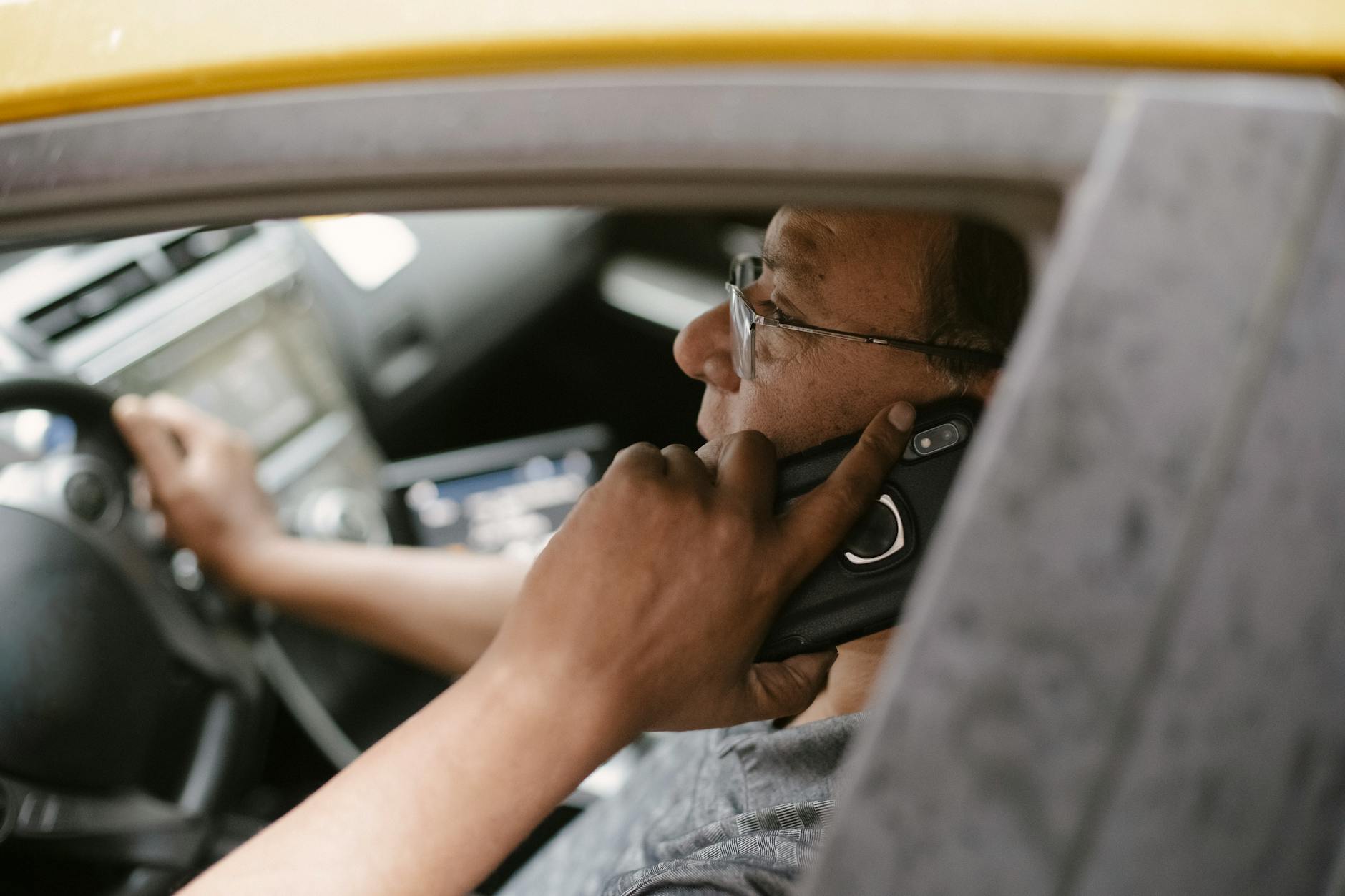 Side view of a taxi driver talking on a phone while driving through the city.