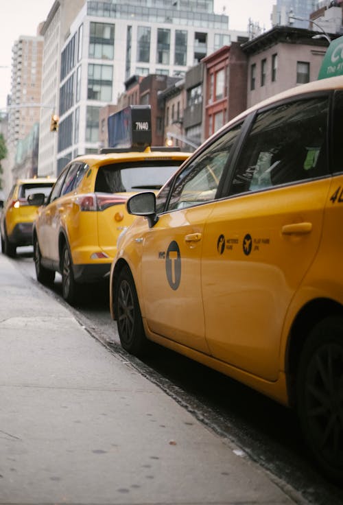 Yellow cabs with logo on doors parked in row on asphalt road near sidewalk against residential buildings in city on street