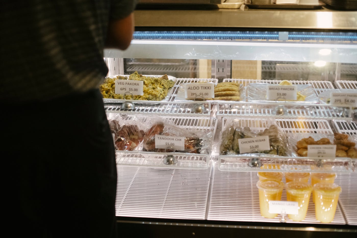 Customer at glass showcase choosing Indian snacks