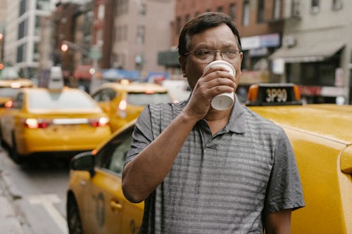 Thoughtful Asian man drinking coffee near cab