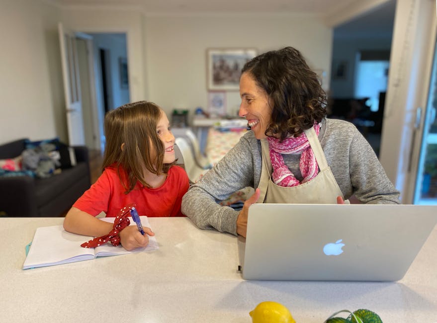 A mother and daughter enjoy homeschooling indoors with a laptop and notebook in a cozy setting.