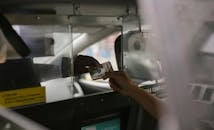 View through open window of unrecognizable driver accepting payment in cash from crop customer sitting on back seat