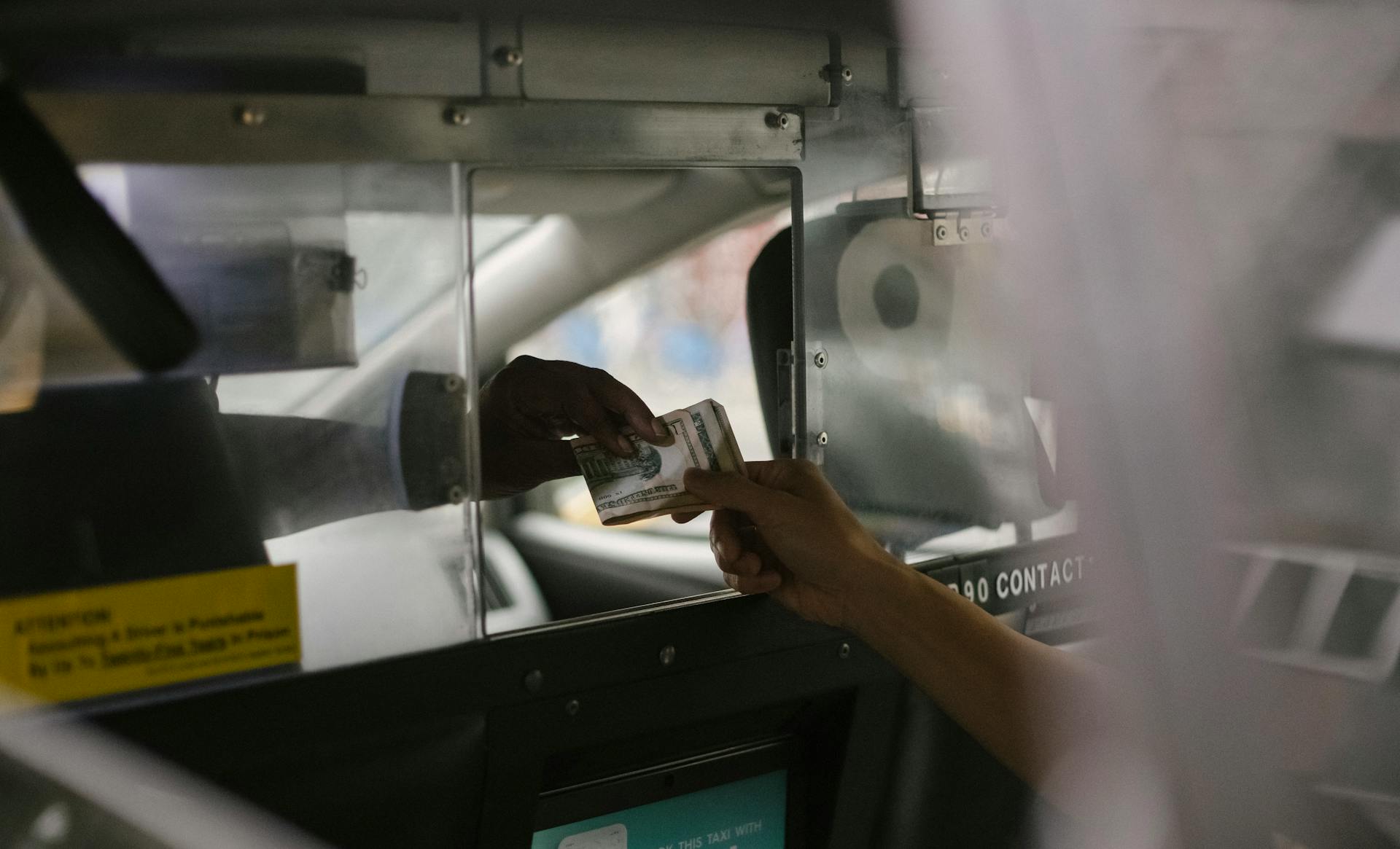 View through open window of unrecognizable driver accepting payment in cash from crop customer sitting on back seat