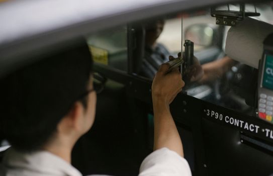 一位穿着白衬衫的年轻男乘客坐在车里，从高处把钱递给司机