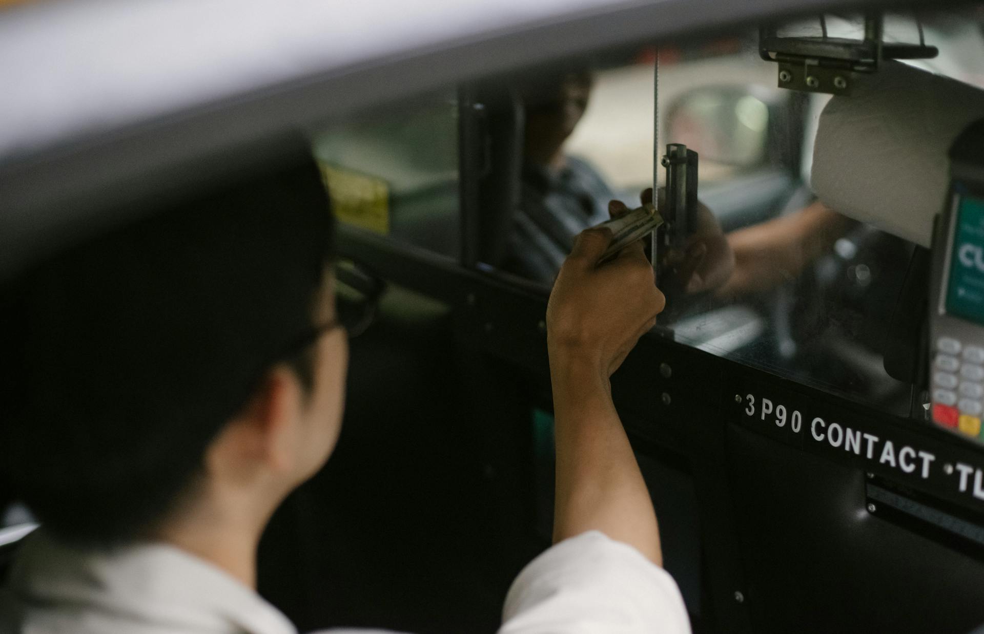 High angle of crop young male passenger in white shirt sitting in automobile and giving dollars to driver