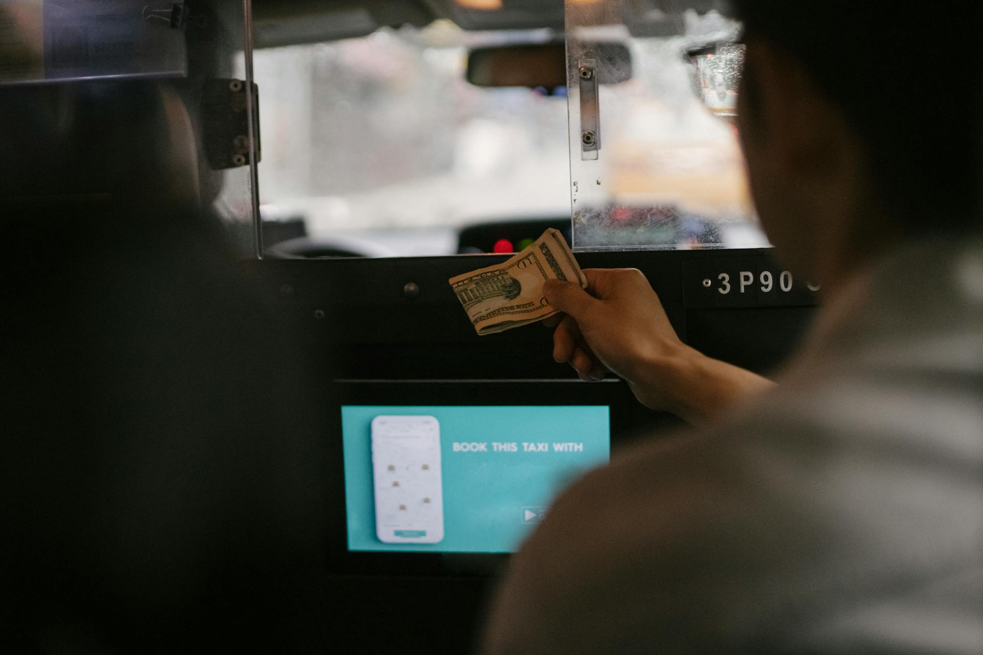 Back view of taxi car interior with tablet screen located near passenger seat and client paying for ride