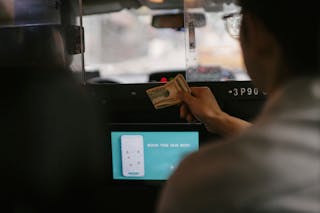Back view of taxi car interior with tablet screen located near passenger seat and client paying for ride