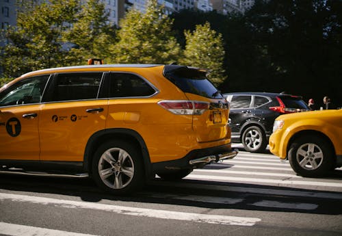 Yellow taxi cars and black SUV driving along road with pedestrian crossing in city centre on summer sunny day