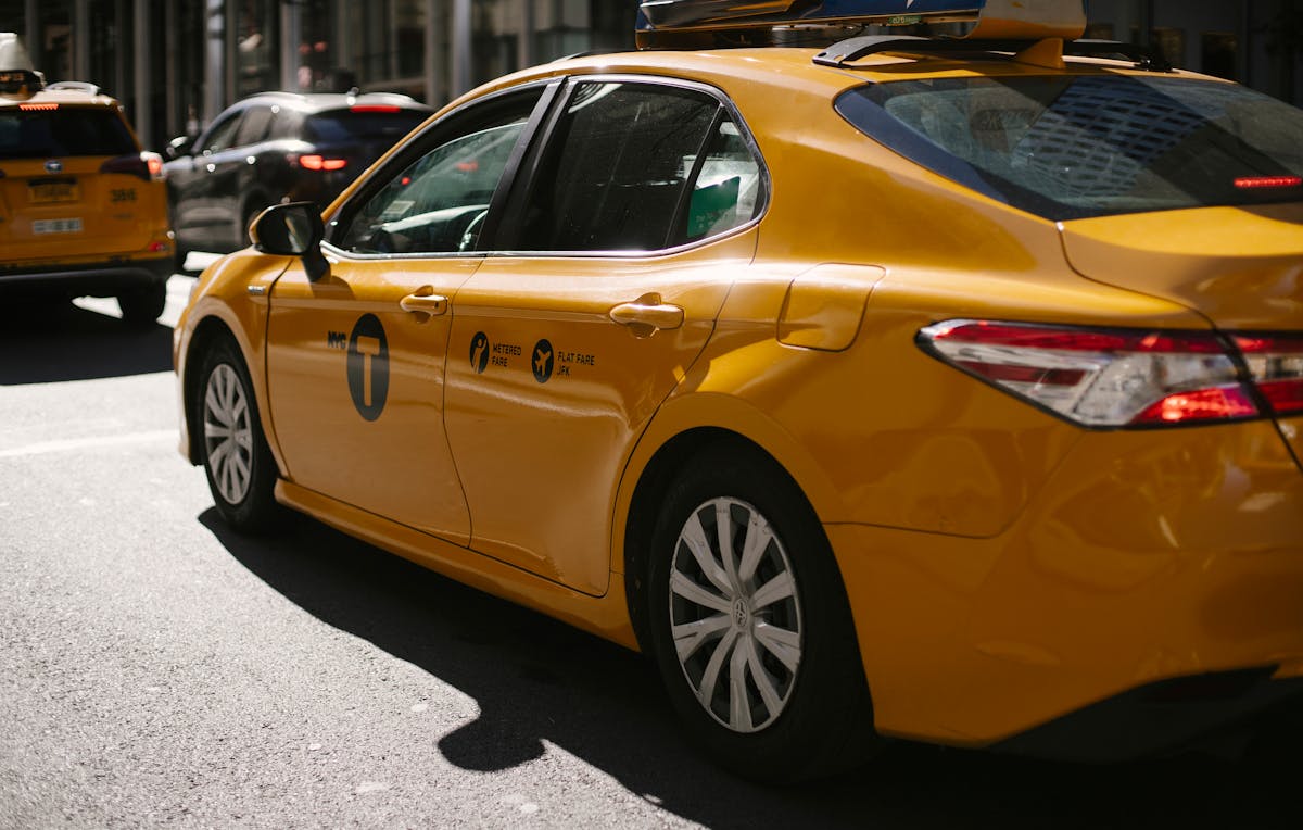Shiny yellow taxi driving along busy street in downtown