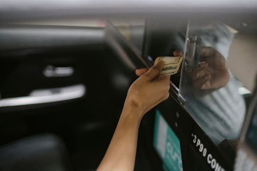 A passenger hands cash to a taxi driver through a window as payment.