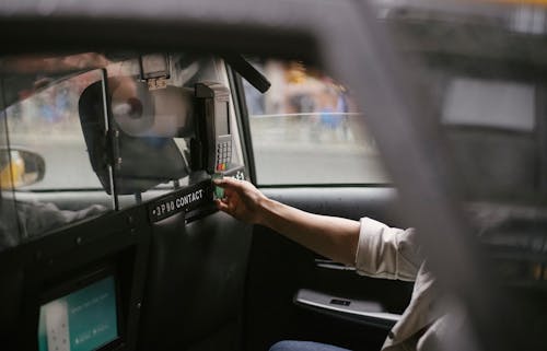 Free Side view of crop faceless male passenger sitting on backseat and using credit card reader to pay for trip in taxi Stock Photo