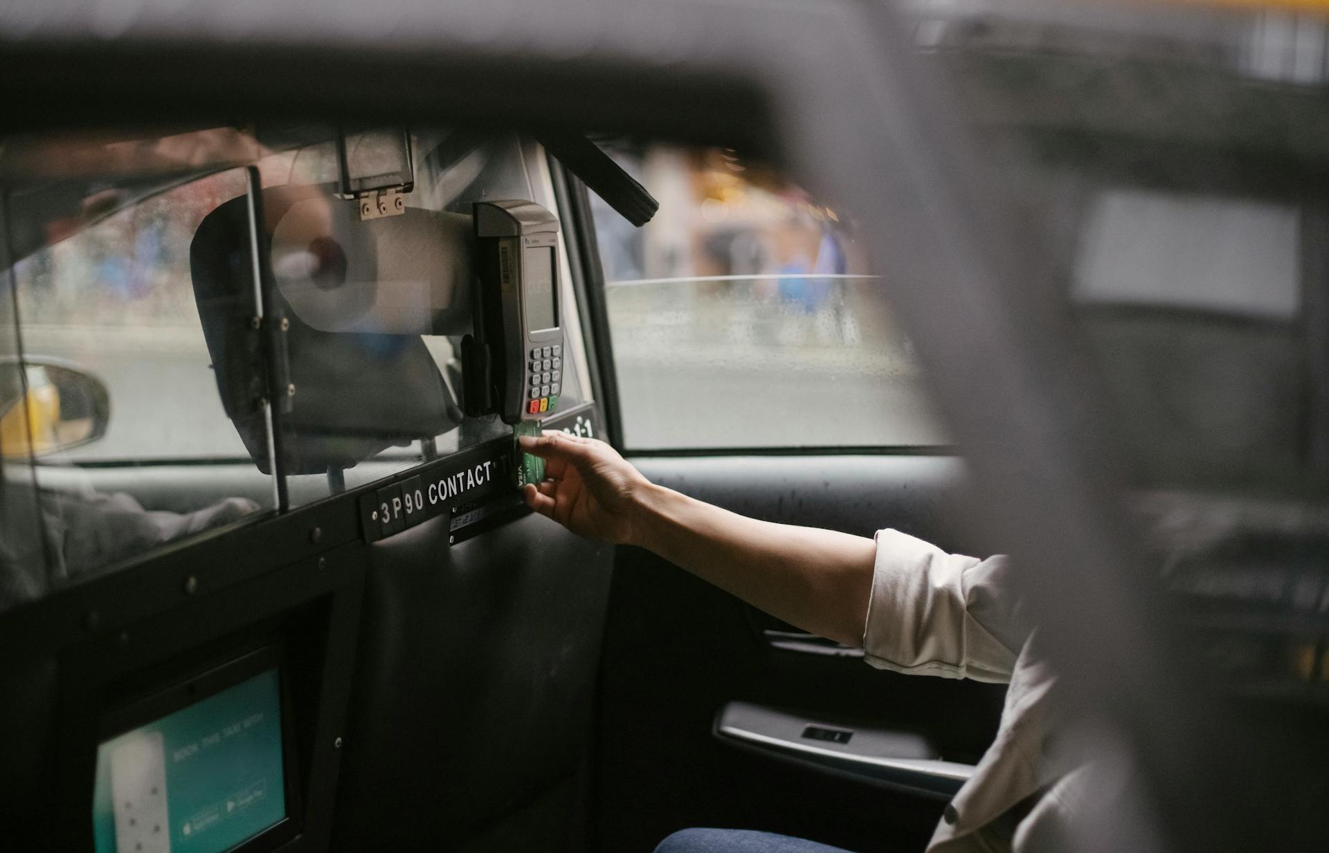 Side view of crop faceless male passenger sitting on backseat and using credit card reader to pay for trip in taxi