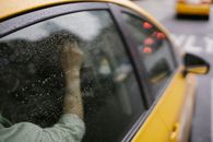 Crop anonymous passenger sitting in yellow taxi car on road in town in rainy weather