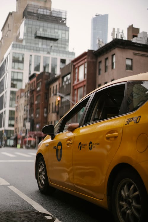 Yellow taxi car ridding on carriageway on street with buildings in town in daytime