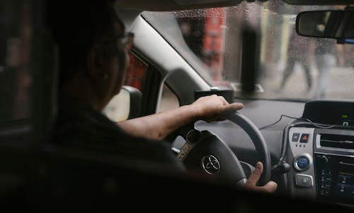Back view of crop anonymous man in eyeglasses driving car in rainy day