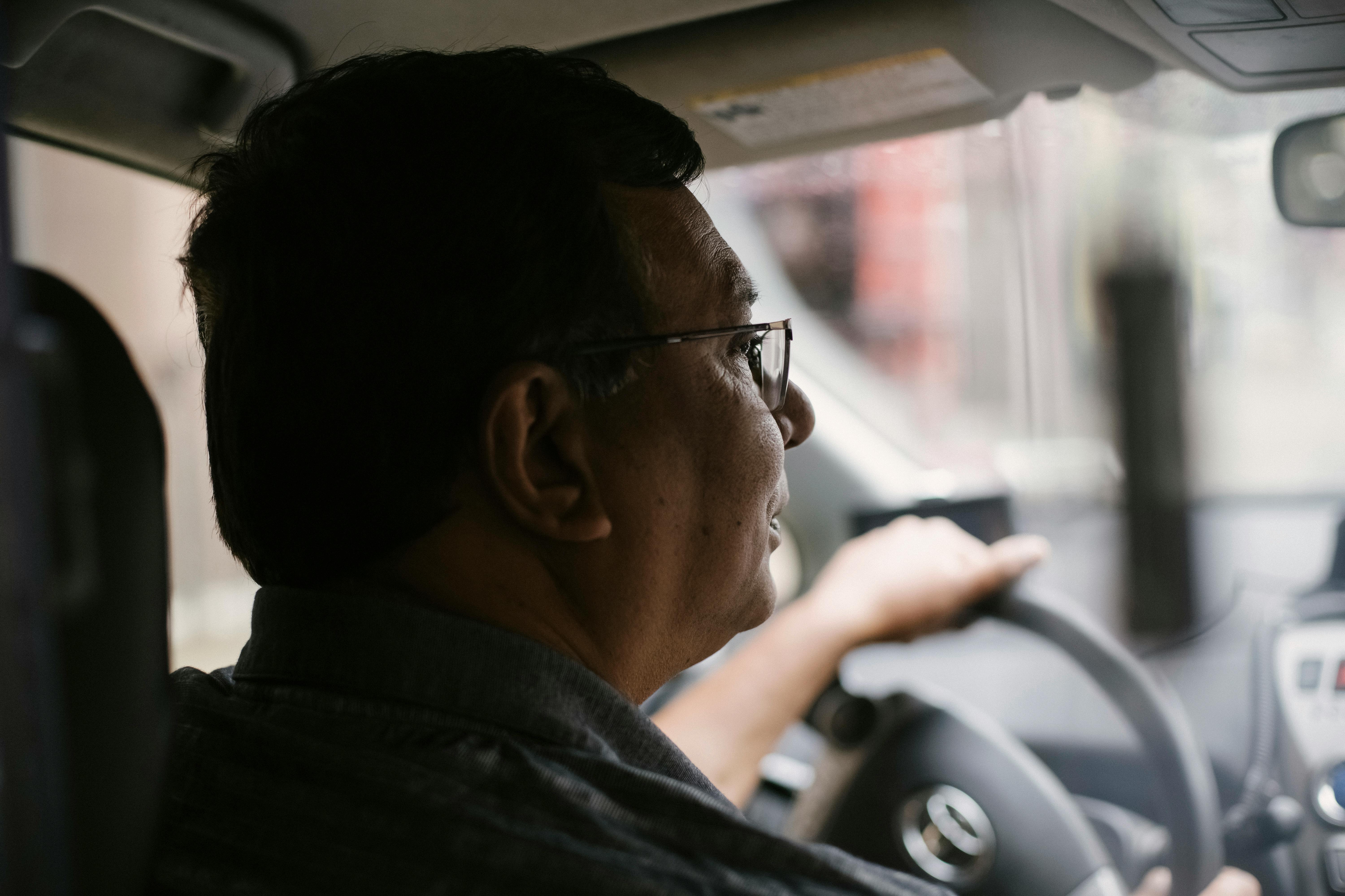 Side view of focused aged male with glasses driving automobile on street on urban background in soft daylight