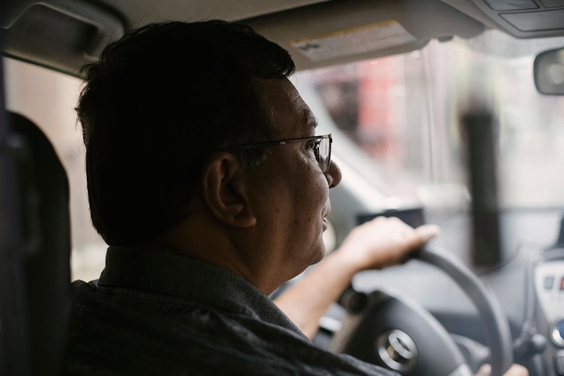Free Side view of focused aged male with glasses driving automobile on street on urban background in soft daylight Stock Photo