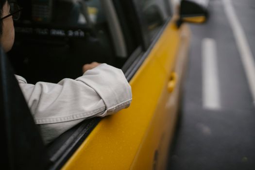 一名穿着衬衫、戴着眼镜的男子身份不明，他坐在黄色出租车里，在柔和的阳光下移开了目光