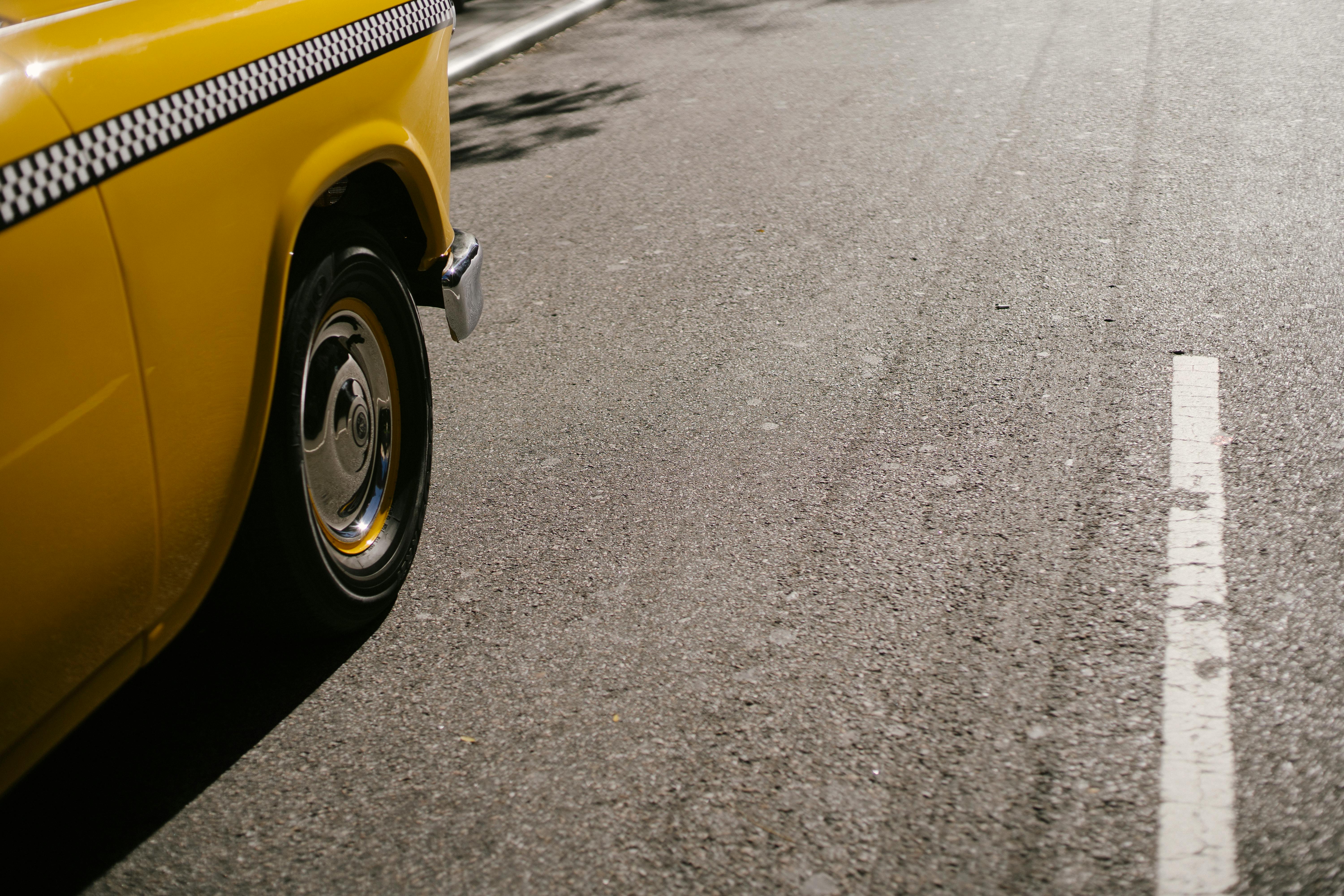 yellow taxi driving on asphalt road