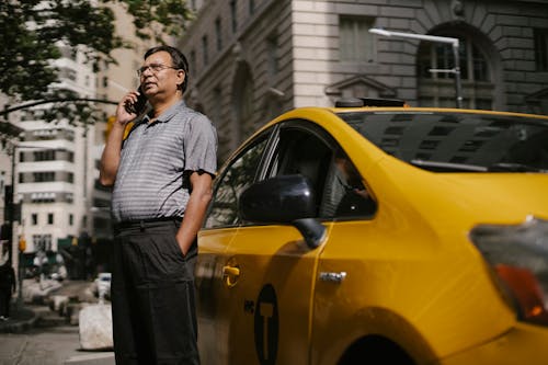 Free Ethnic male in eyeglasses holding hand in pocket while standing on street and talking on phone Stock Photo