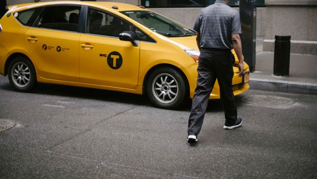 一名男子走过一辆停靠在城市街道上的黄色纽约出租车